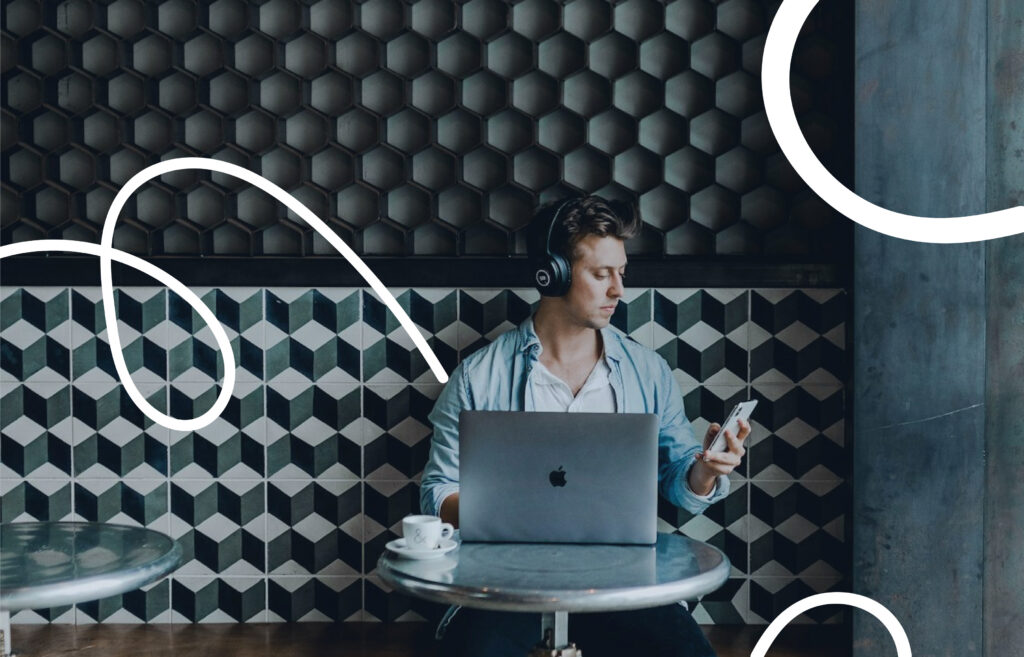 Person wearing headphones working on a laptop at a café table while checking a phone, with abstract white line graphics overlayed.